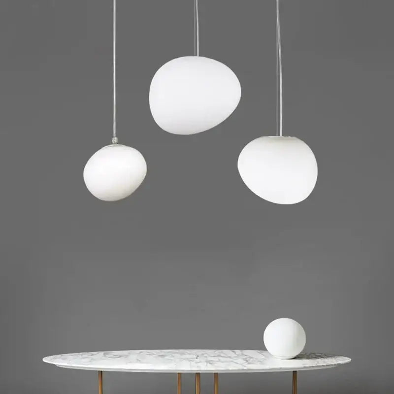 Three white glass ball led pendant lights with frosted glass shades hang above a marble dining table decorbites pendant light