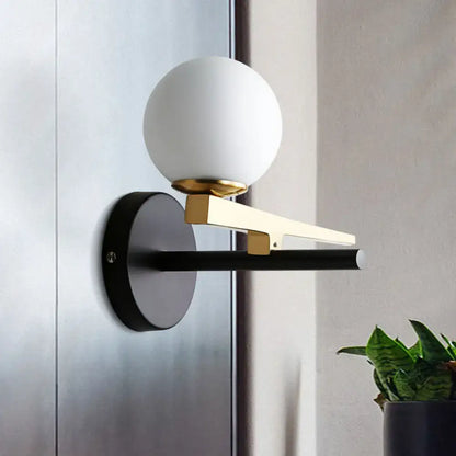 Modern white glass sphere wall light with gold accents and black base single light for bedroom use