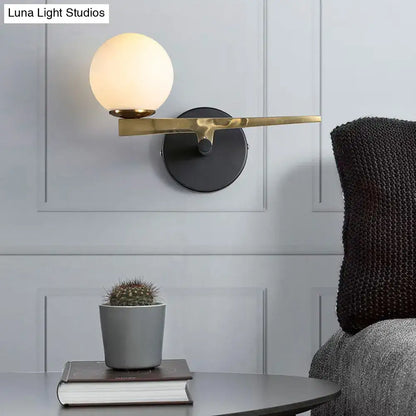 Modern brass wall light with frosted white glass globe shade featuring gold and black single light design for bedroom