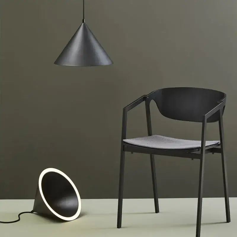 Black minimalist chair with sleek frame and gray upholstered seat next to modern white and gold decorbites annular cone pendant lamp