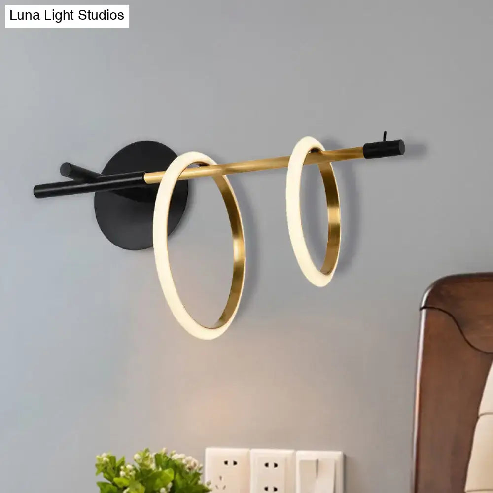 Modernist wall light with two glowing white and gold circular rings in brushed gold on a sleek black base