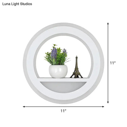 Modern white halo ring wall light fixture with glossy circular shelf holding purple flowers and eiffel tower figurine