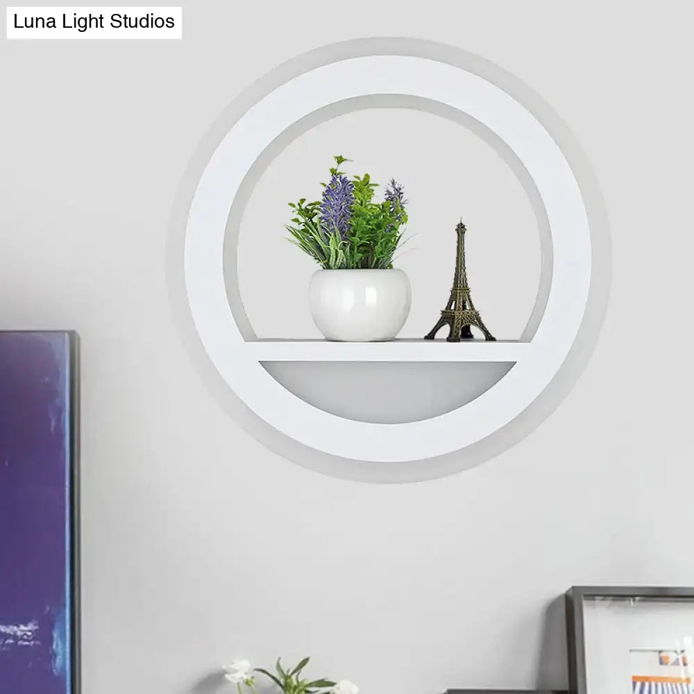 Modern white halo ring wall light fixture with glossy circular shelf holding white ceramic pot and miniature eiffel tower