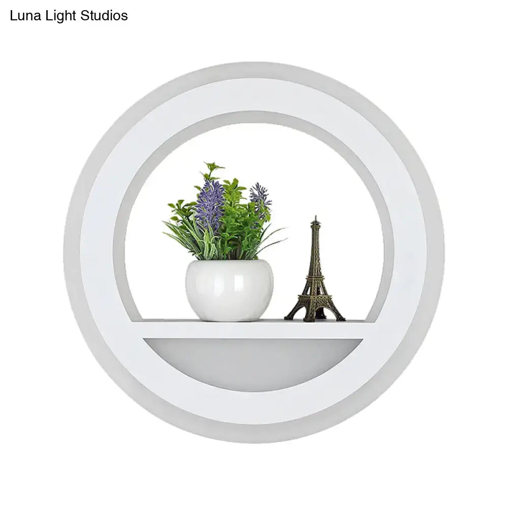 Modern white halo ring wall light fixture with circular shelf holding ceramic pot with purple flowers and eiffel tower figurine