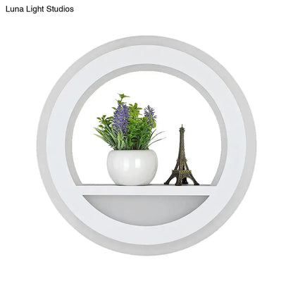 Modern white halo ring wall light fixture with circular shelf holding ceramic pot with purple flowers and eiffel tower figurine