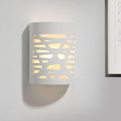 Modern white cylindrical wall sconce with geometric cutout pattern casting warm light from led light bulb