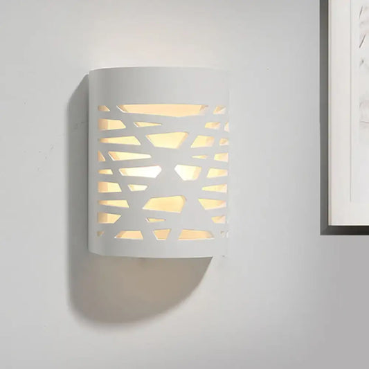 Modern white cylindrical wall sconce with geometric cutout pattern casting warm light from led light bulb