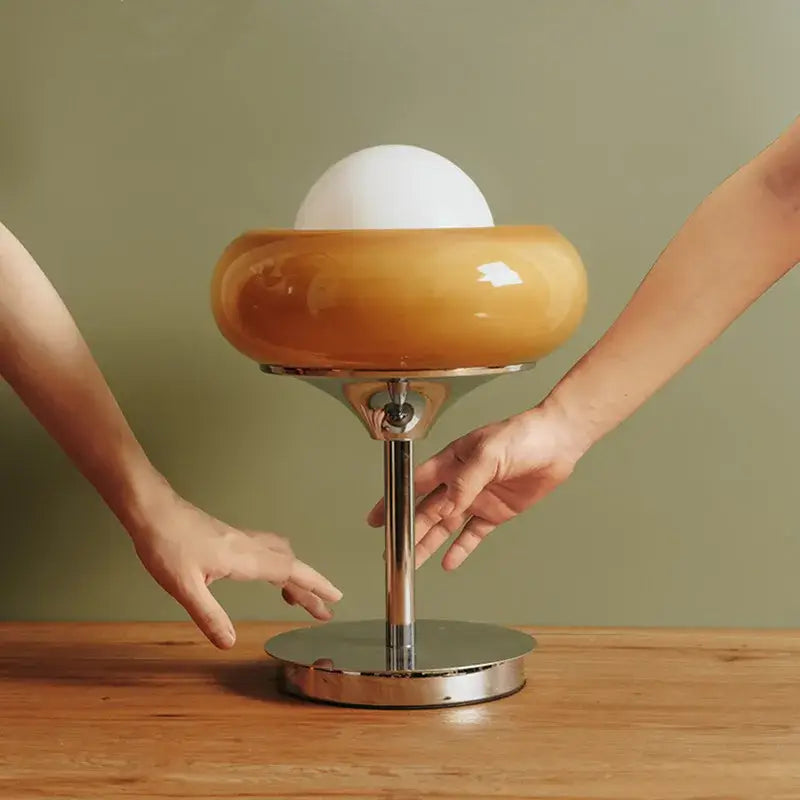 A modern yellow and chrome glass egg tart desk lamp with a glossy amber glass shade and polished chrome base