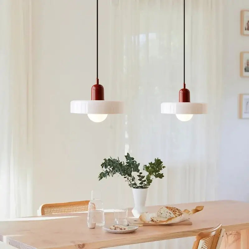 Two modern pendant lights with red glass tops and white shades hanging above a wooden dining table chandelier pendant light