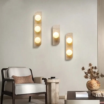 Three modern yellow travertine led wall lamps with warm glowing bulbs set in textured stone panels for bedroom lighting