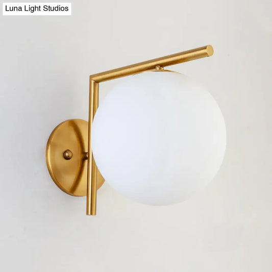 Modernist gold and white globe sconce light with frosted glass shade and geometric metal frame for bedroom wall use