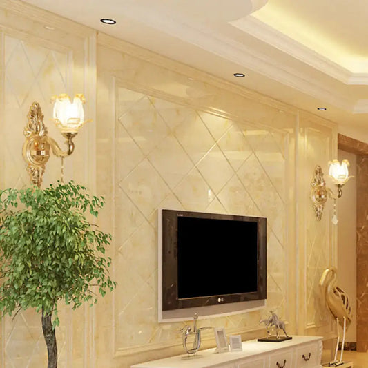 Modernist gold wall sconce with glass shade and direct wired electric next to a sleek black flat-screen tv on beige marble wall