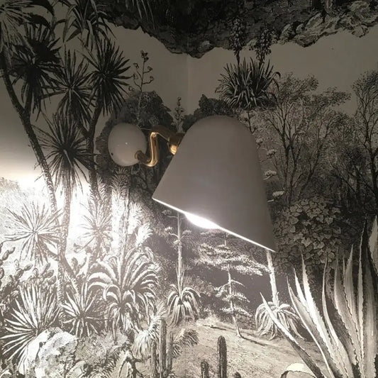 A modernist off-white conical wall mounted sconce with gold finished arm and rotating node for wide flare bedroom light