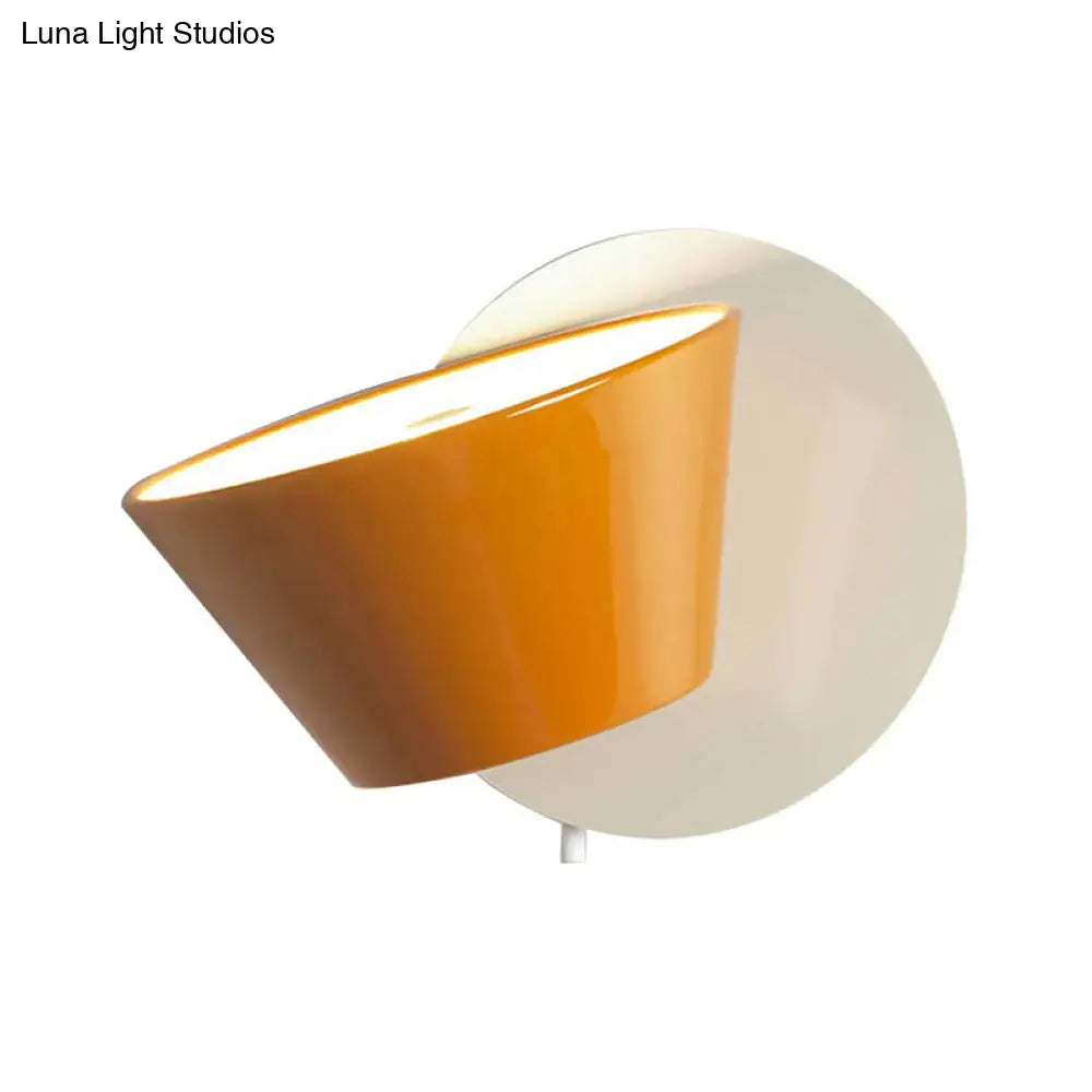 Modernist wall lamp with orange barrel metal shade and glossy finish mounted on circular white backplate for bedroom lighting