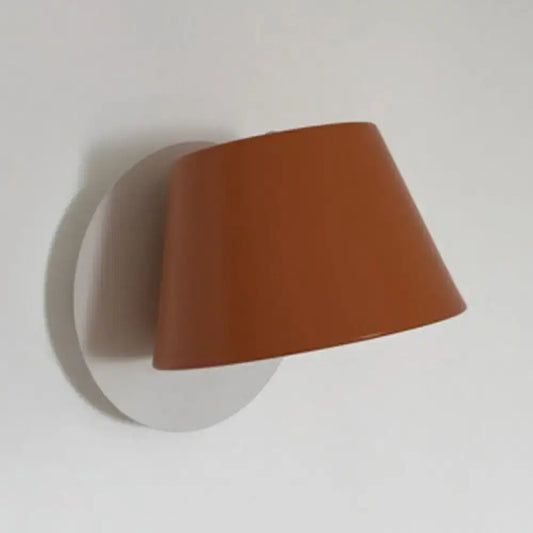 A sleek terracotta wall lamp with an orange metal shade and minimalist conical design for bedroom lighting