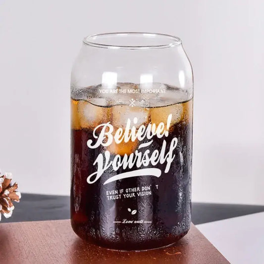 Clear glass shape beer glass cup filled with iced dark soda featuring white engraved motivational text believe yourself