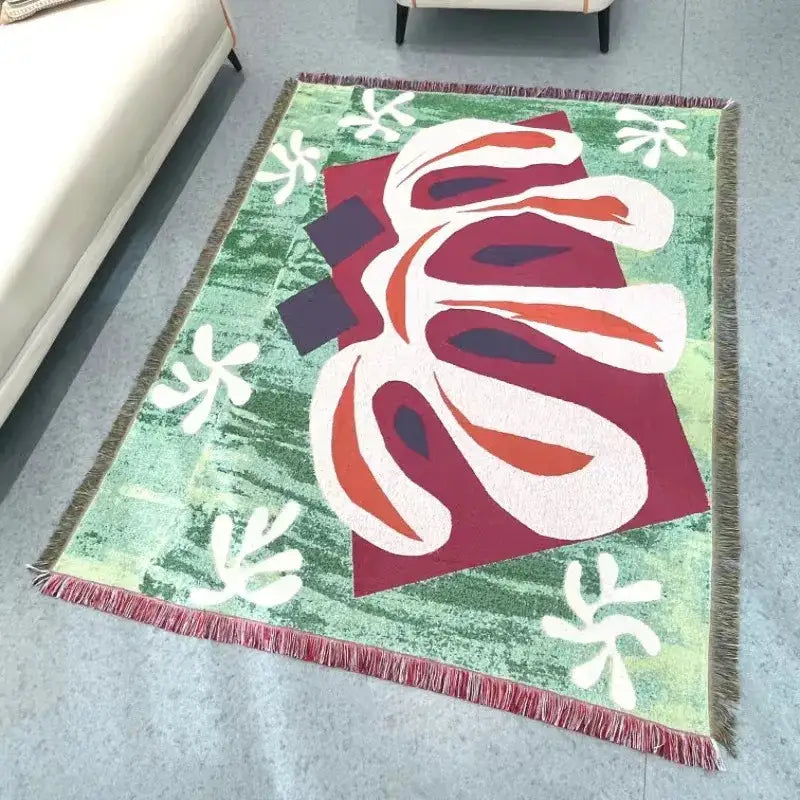 A vibrant green jacquard tapestry blanket with bold white red maroon abstract shapes and fringe edges for living room use