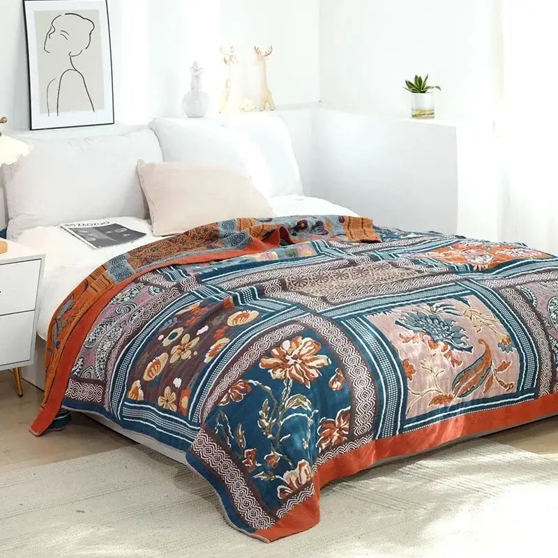A multicolored cotton gauze boho throw blanket featuring a patterned patchwork in deep teal and burnt orange decorbites cotton gauze