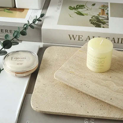 A pale yellow cylindrical candle on a decorbites beige travertine marble plate kitchen and bathroom tray