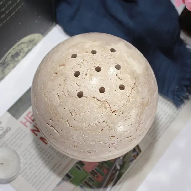 Beige travertine spherical incense burner with evenly spaced circular perforations for living room decor by decorbites