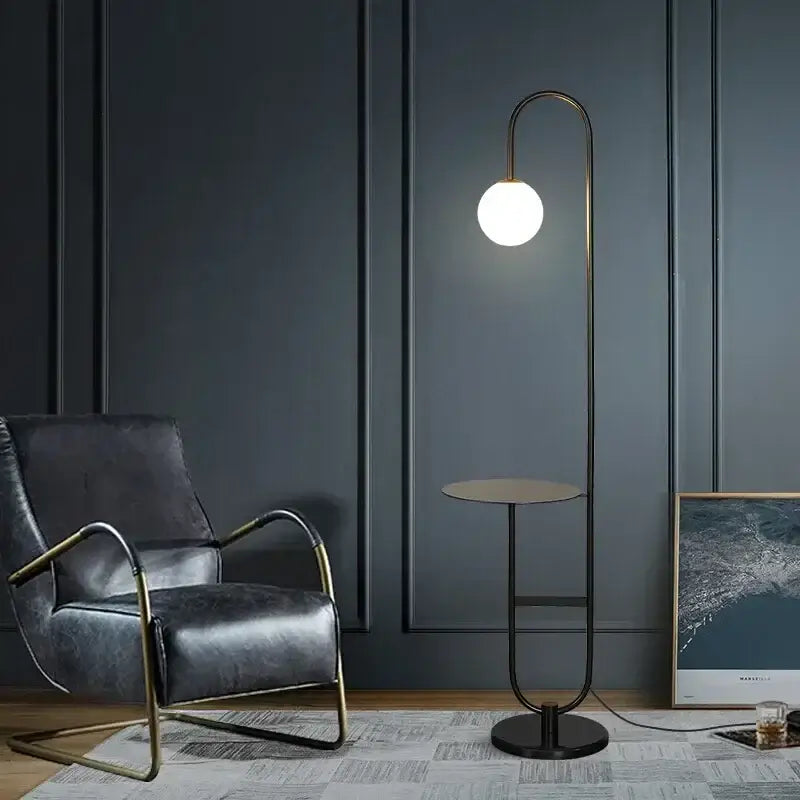 Modern floor lamp with a curved brass frame and glowing white bulb beside a Nordic black metal led floor lamp with glass table