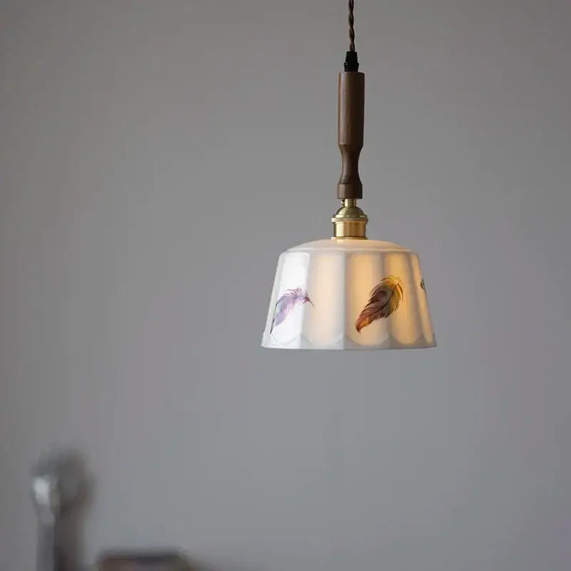 A delicate white ceramic pendant light with hand-painted feathers and decorbites brown wood led fixture for dining room