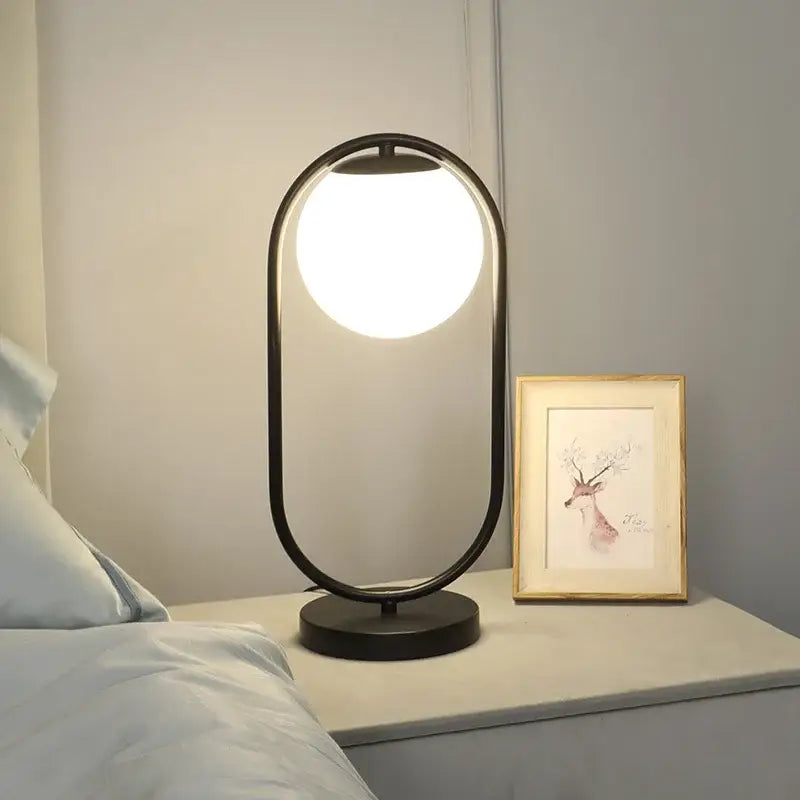 Modern black metal table lamp with glowing circular bulb and sleek oval frame featuring decorbites glass ball LED design