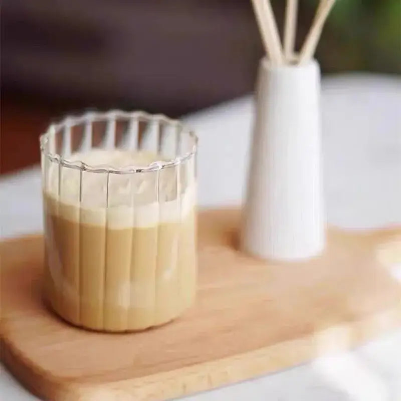 A clear ribbed glass ripple cup with creamy coffee and gold leaf spoon on wooden tray nordic design dining room