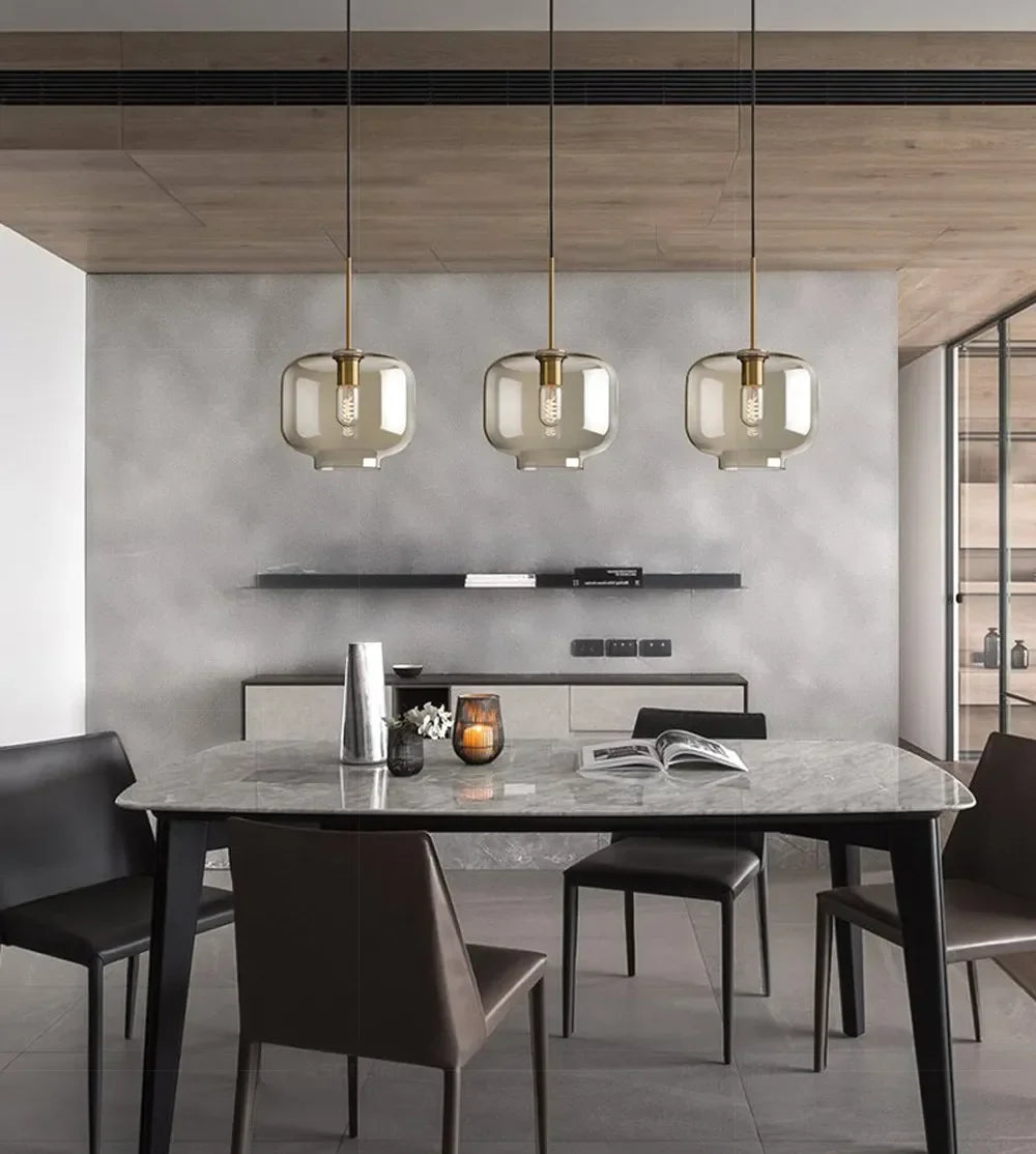 Three modern nordic led glass pendant lights with smoked glass shades and brass accents hang above a dining room table