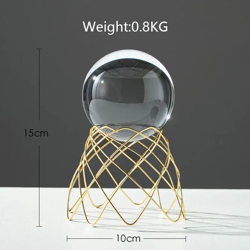 A clear crystal ball crafts resting on a gold-toned wireframe stand showcasing nordic light luxury decor