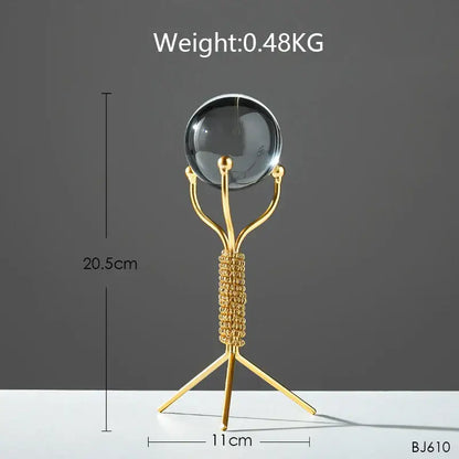 A nordic light luxury gold crystal ball craft features a sleek metal stand with a knotted design supporting a dark glass sphere