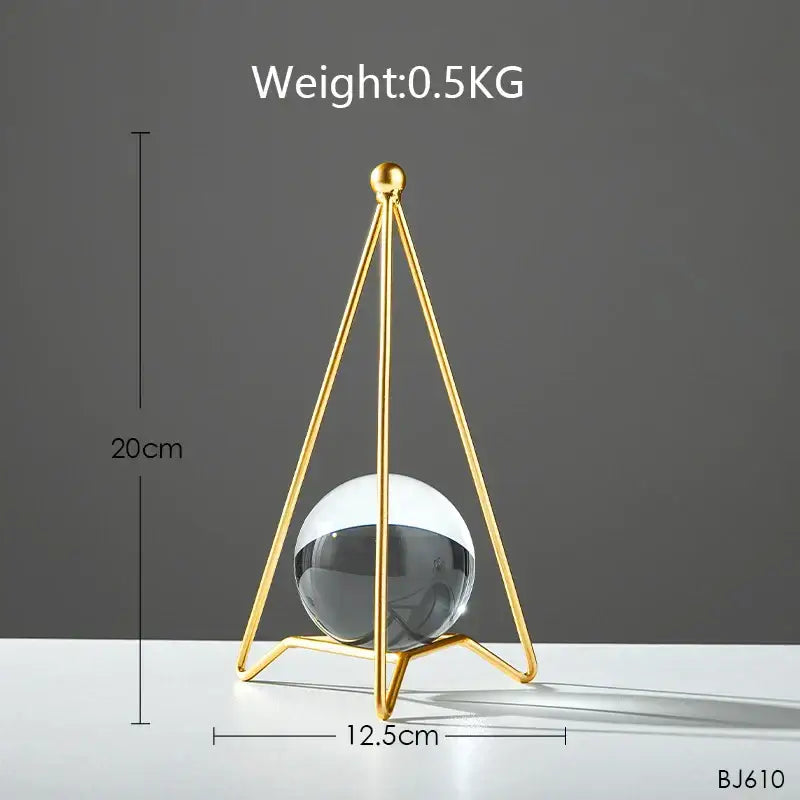 A sleek gold-toned metal tripod stand cradles a translucent reflective black and white crystal ball for nordic light luxury decor