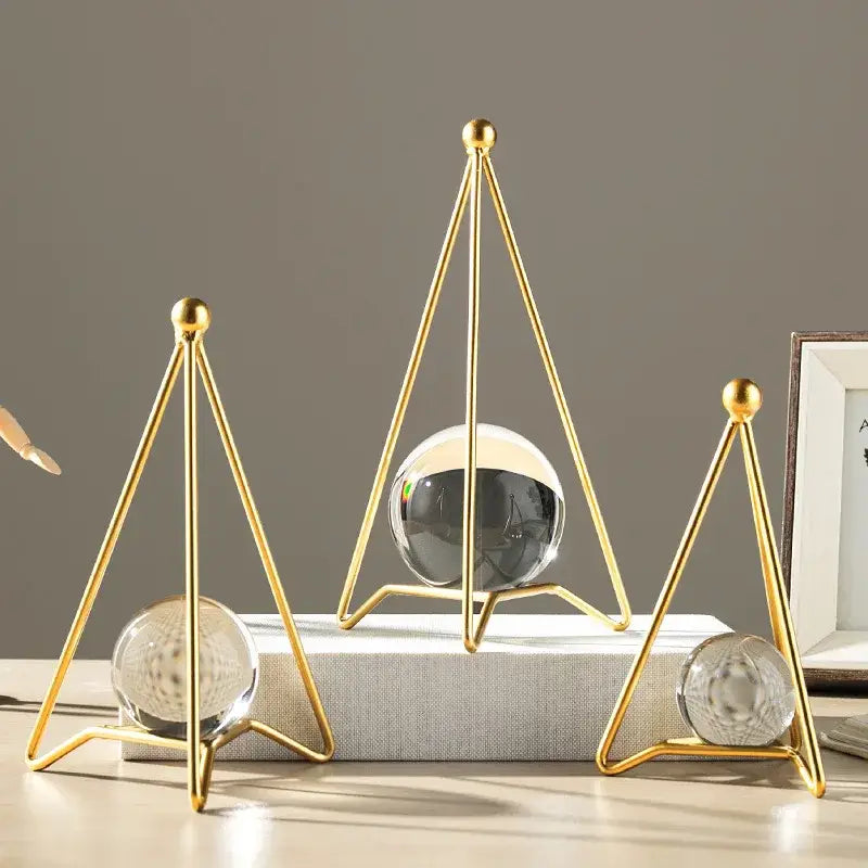 Gold-toned triangular metal stands holding clear and dark crystal ball crafts for nordic light luxury decor