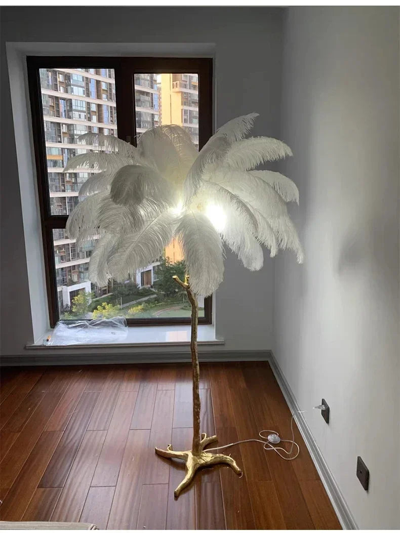 A tall feather floor lamp with white ostrich feathers and a gold base for living room home decor and bedside lighting