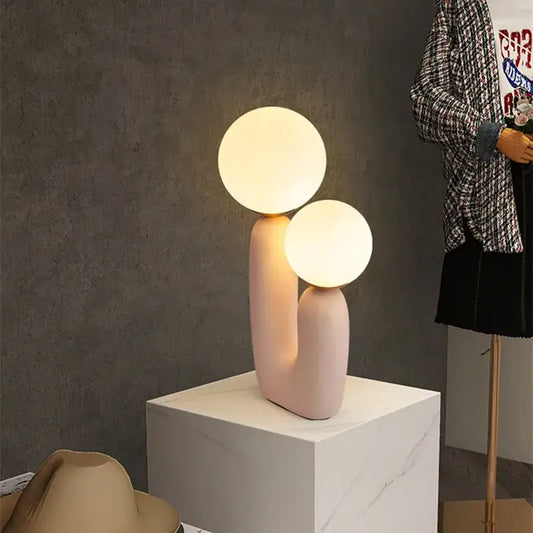 Pastel pink ceramic ball table lamp with two glowing spherical bulbs for bedroom decor in nordic style