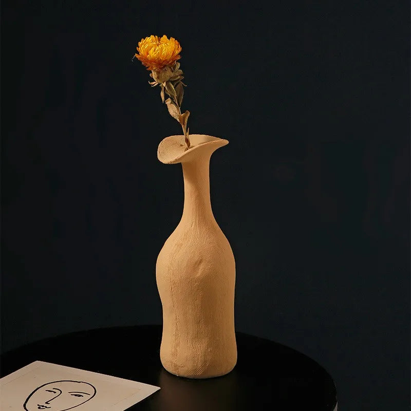 A beige ceramic morandi color vase with textured surface and flared opening holding a dried yellow flower for nordic home decoration