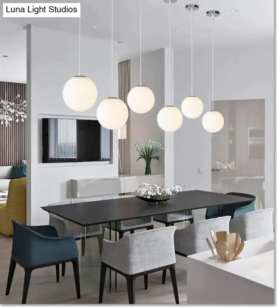 Six nordic white glass ball pendant lights with frosted finish hanging in a modern dining room setting