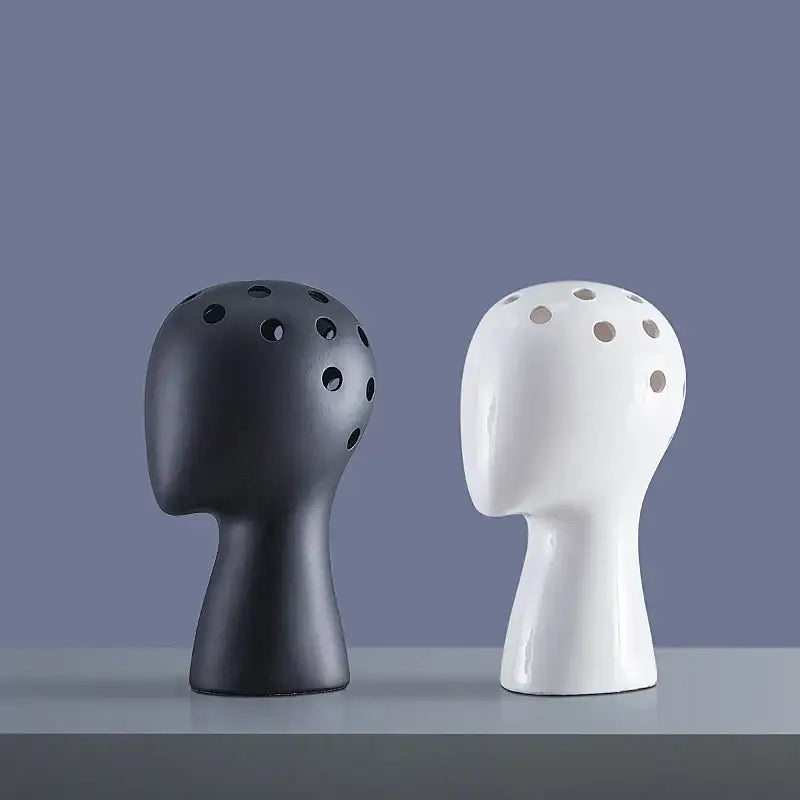 Two minimalist ceramic vases in human head shape with circular perforations in matte black and glossy white decorbites design
