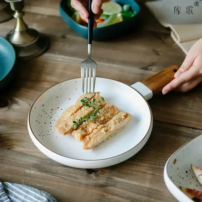 Nordic white speckled ceramic wood handle bowl with gold rim holding sliced fried chicken garnished with fresh herbs