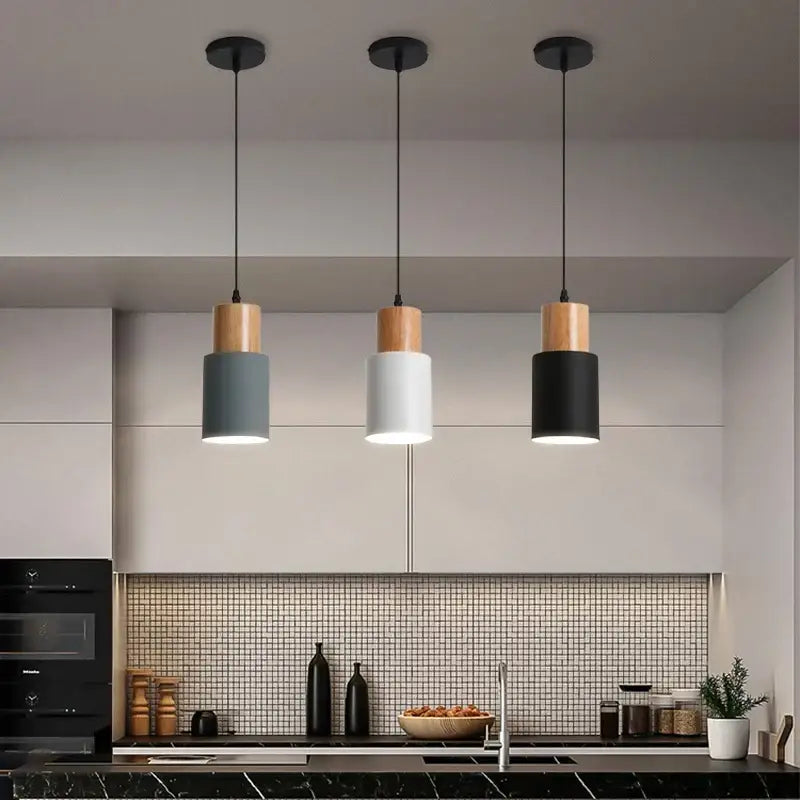 Three modern pendant lights with cylindrical gray white and black shades and solid wood top caps for kitchen or dining room