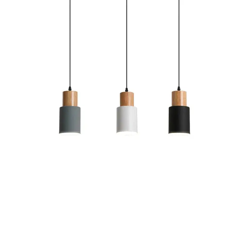 Three minimalist pendant lights with solid wood tops and cylindrical shades in gray white and black for kitchen use