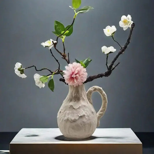 Off-white handmade irregular grain ceramic pitcher vase with handle holding delicate white and pink blossoms decorbites