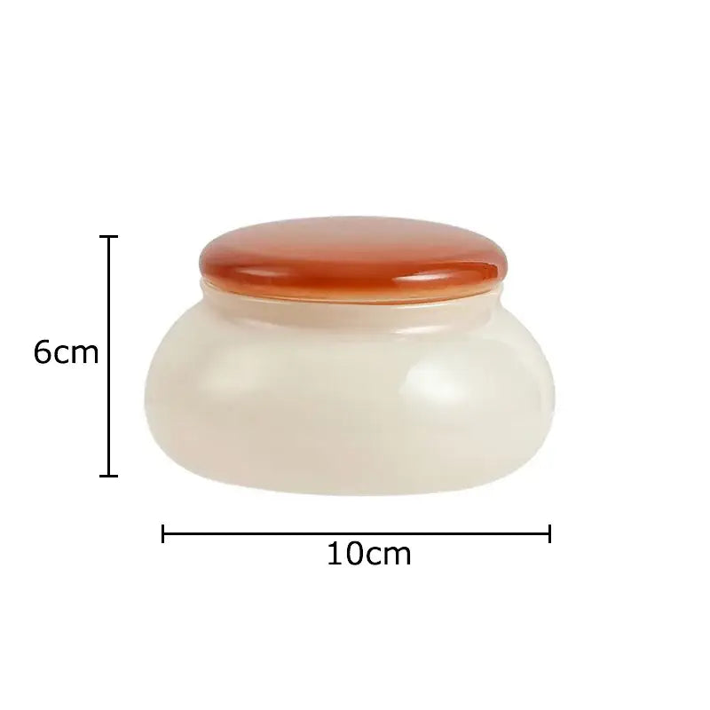A smooth white ceramic storage jar with a glossy amber lid in the orange and blue glass storage jar set