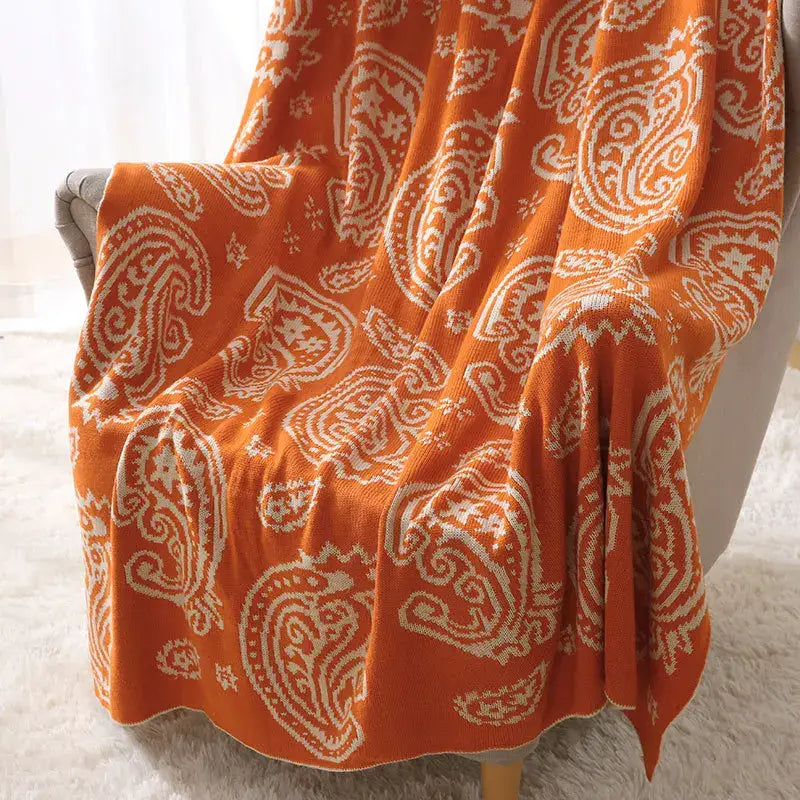Orange knit throw blanket with white decorbites cashew pattern draped over chair for living room decor
