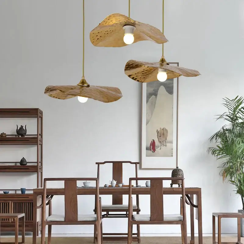 Three golden iron lotus leaf pendant lights with perforated design hang above wooden dining table decorbites golden iron