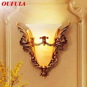 Ornate gold glass sconce light with warm amber shade, crystal accents, and intricate scrollwork wall lamp for living room