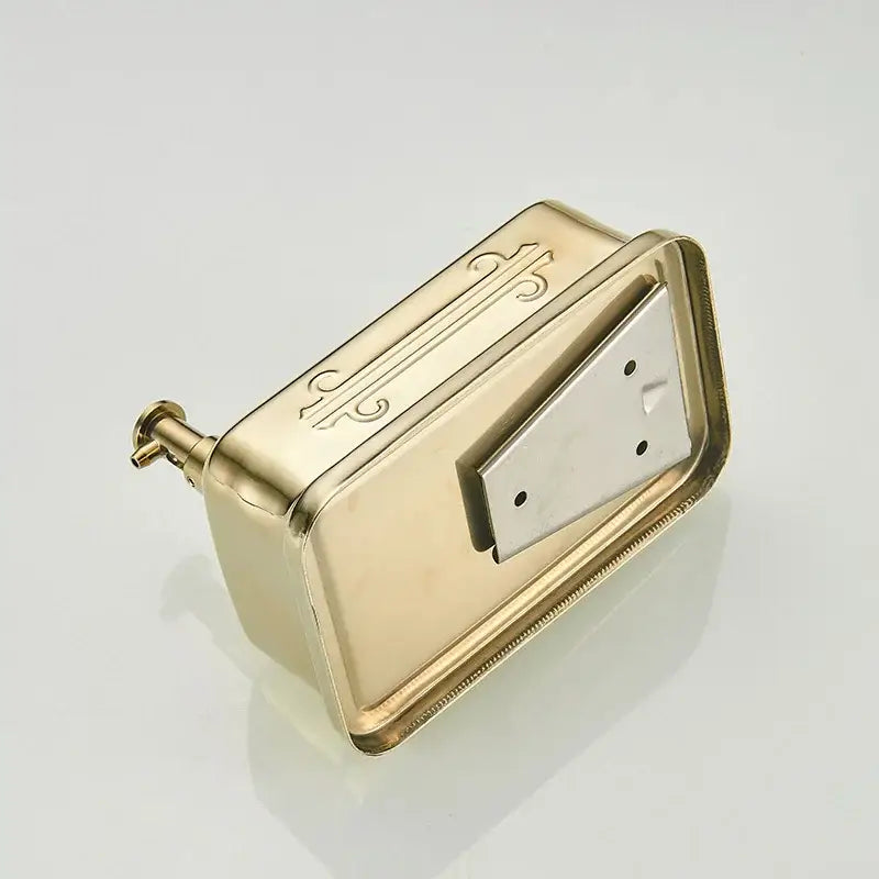 Ornate gold stainless steel soap dispenser with decorative engraved patterns and silver toned triangular flap wall mount