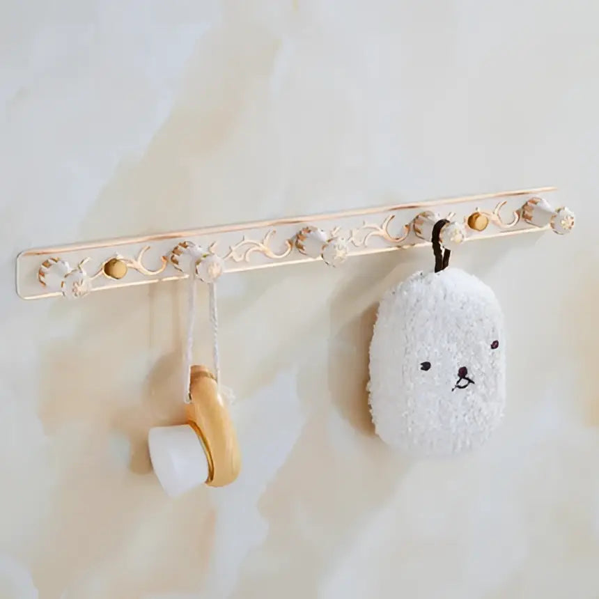 Ornate gold and white floral wall-mounted towel rack with decorative knobs holding a bunny loofah in decorbites bathroom accessories set