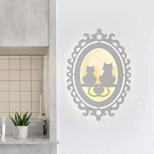 Elegant gray ornate wall light fixture with two cat silhouettes seated on heart-shaped ledge illuminated warm yellow light