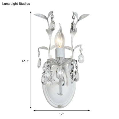 Ornate white metal wall light fixture with silver crystal leaf and teardrop accents for bedroom sconce lighting